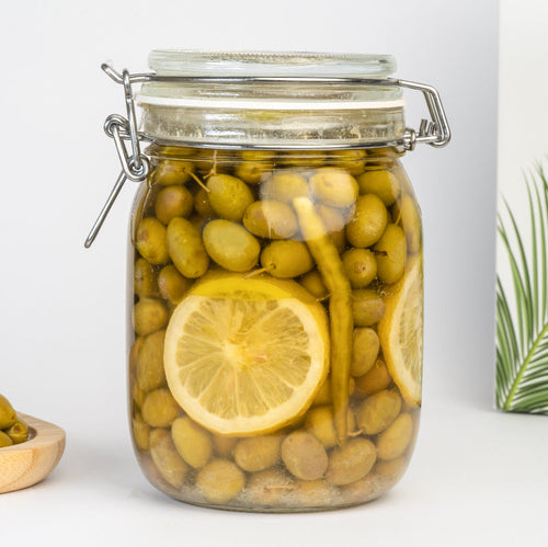 Jar of pickled green olives with lemon slices on a white background